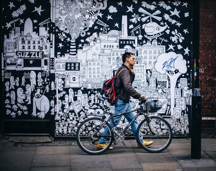 Man walking a bicycle past a detailed urban graffiti mural in a city setting.